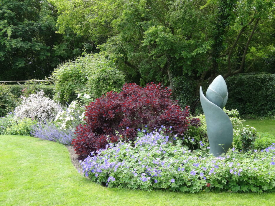 Sculpture of an Iris Bud by Anne Curry shown in a flower border