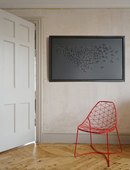 Abstract artwork in grey leather by Louise Heighes shown framed and mounted on a wall