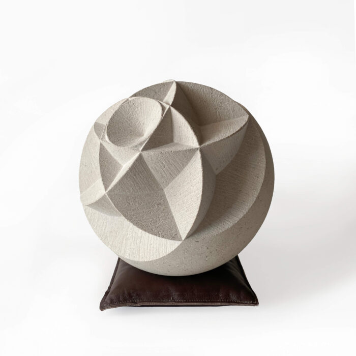 Portland-stone-ball-hand-carved-with-deep-geometric-pattern-resting-on-leather-sandbag-by-artist-Zoe-Wilson-for-sale-with-Guilded